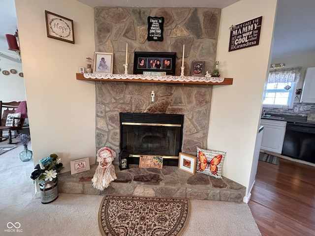 interior details featuring a stone fireplace, sink, decorative backsplash, hardwood / wood-style flooring, and dishwasher