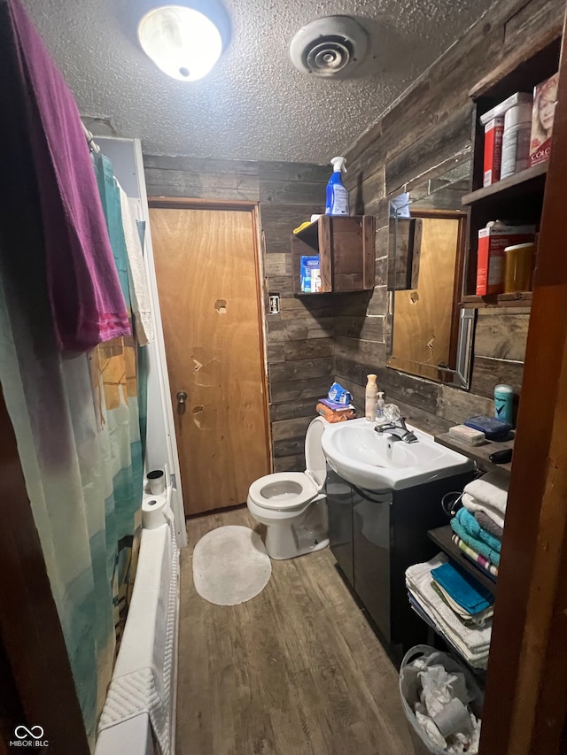 bathroom featuring wood-type flooring, a textured ceiling, wooden walls, a shower with curtain, and vanity