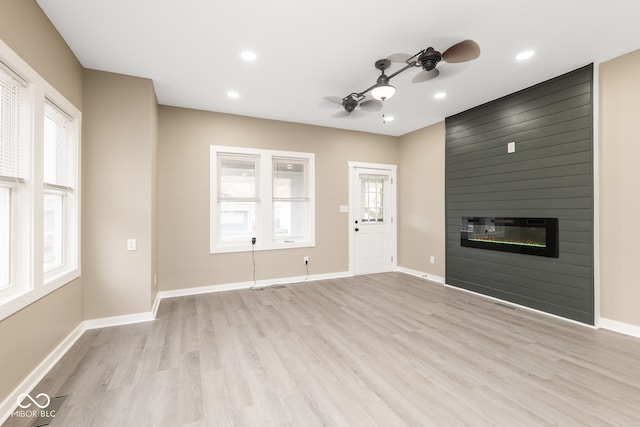 unfurnished living room with light wood-type flooring, a large fireplace, and ceiling fan