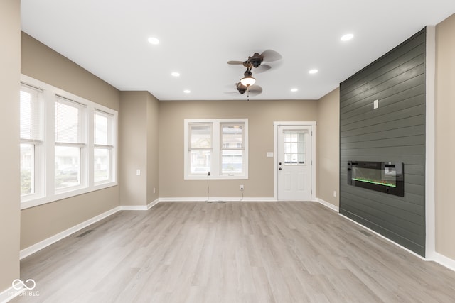 unfurnished living room featuring a large fireplace, ceiling fan, and light hardwood / wood-style flooring