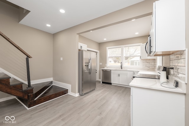 kitchen featuring light wood-type flooring, appliances with stainless steel finishes, backsplash, sink, and white cabinets