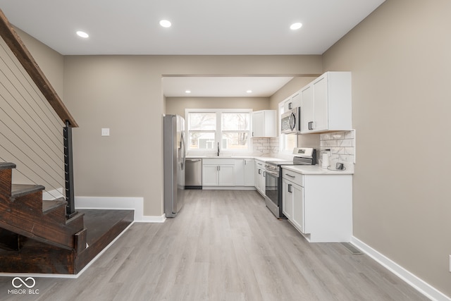 kitchen featuring appliances with stainless steel finishes, decorative backsplash, light hardwood / wood-style floors, and white cabinets