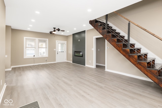 unfurnished living room with light wood-type flooring, a large fireplace, and ceiling fan