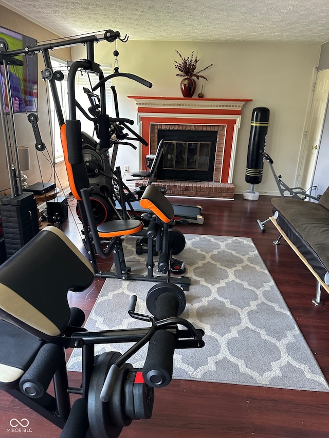 exercise room featuring a brick fireplace, a textured ceiling, and dark hardwood / wood-style flooring