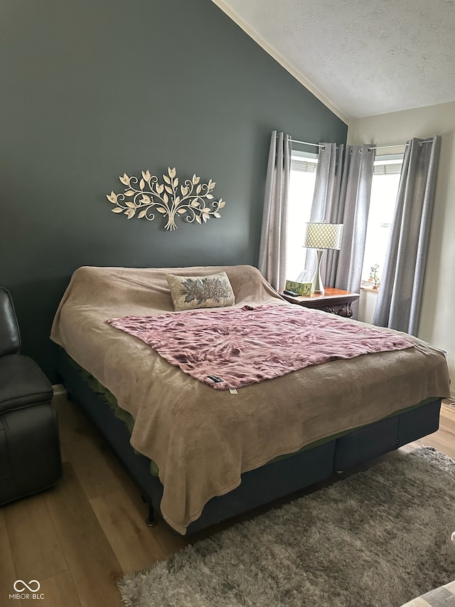 bedroom with hardwood / wood-style floors, a textured ceiling, and vaulted ceiling