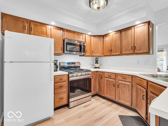 kitchen with sink, a textured ceiling, light hardwood / wood-style floors, and stainless steel appliances