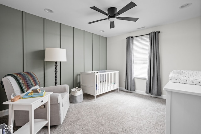 carpeted bedroom with ceiling fan and a nursery area