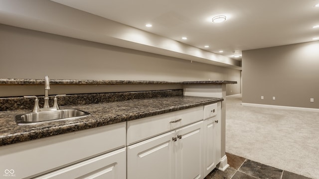 kitchen with dark stone countertops, white cabinetry, sink, and dark colored carpet