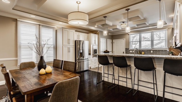 kitchen featuring white cabinets, stainless steel refrigerator with ice dispenser, light stone counters, and hanging light fixtures