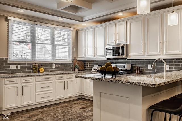 kitchen featuring ornamental molding, decorative light fixtures, stone counters, white cabinets, and a breakfast bar area