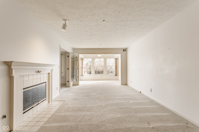 unfurnished living room with light colored carpet, a textured ceiling, and a tile fireplace