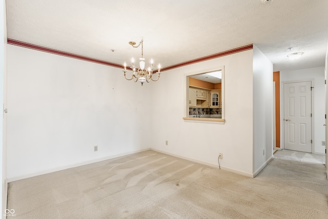 spare room with ornamental molding, a textured ceiling, a notable chandelier, and light carpet