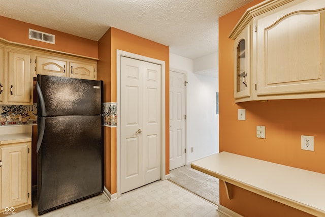 kitchen with light brown cabinetry, black fridge, and a textured ceiling