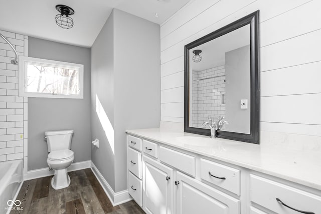 full bathroom featuring tiled shower / bath combo, wood walls, toilet, vanity, and hardwood / wood-style flooring