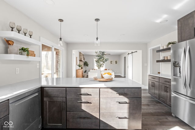 kitchen with a barn door, appliances with stainless steel finishes, decorative light fixtures, dark hardwood / wood-style flooring, and dark brown cabinetry