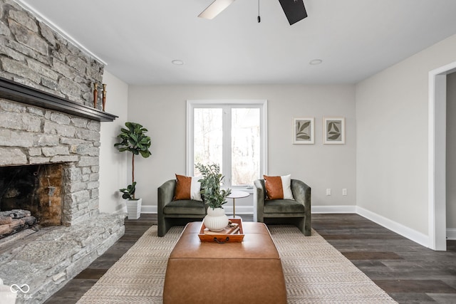 living room with a stone fireplace, ceiling fan, and dark wood-type flooring