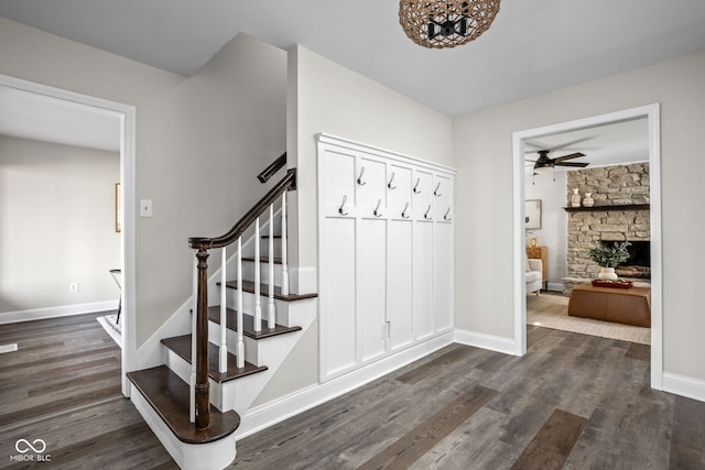 stairs with hardwood / wood-style flooring, ceiling fan, and a stone fireplace