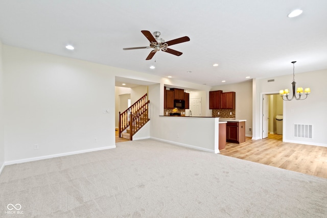 unfurnished living room with ceiling fan with notable chandelier and light colored carpet