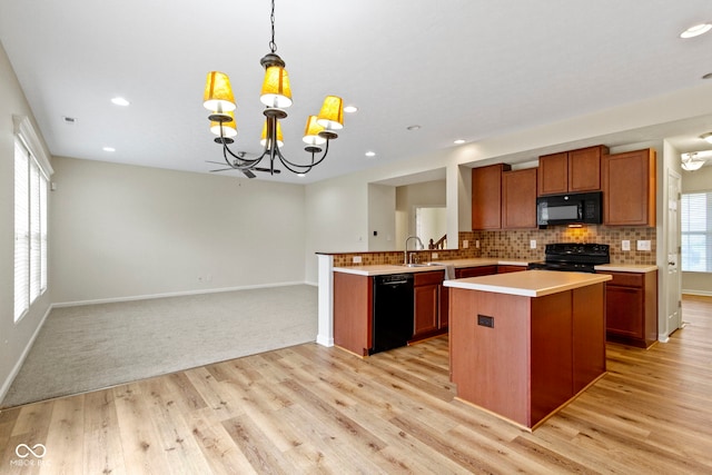 kitchen featuring black appliances, hanging light fixtures, light hardwood / wood-style floors, kitchen peninsula, and a chandelier