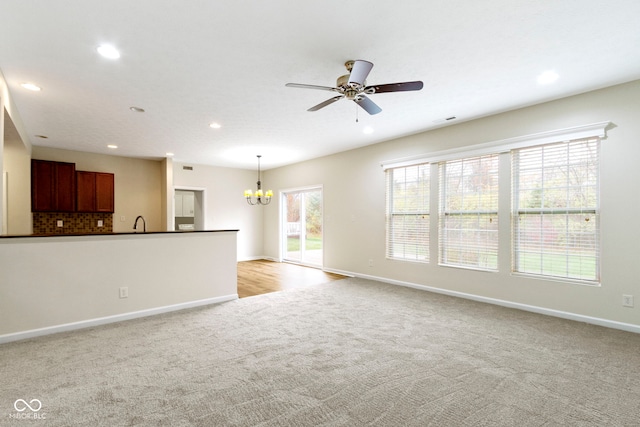 unfurnished living room featuring ceiling fan with notable chandelier, sink, and light carpet