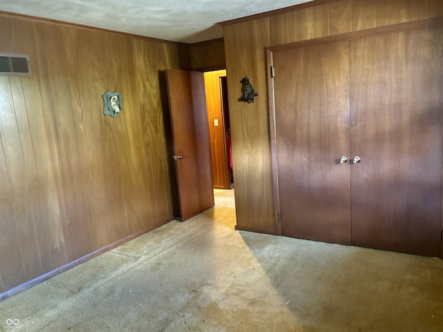 unfurnished bedroom with wood walls, light carpet, a textured ceiling, and a closet