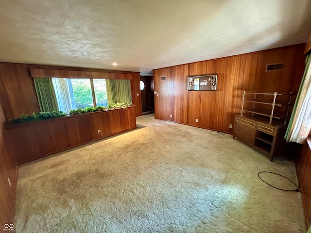 unfurnished living room featuring wood walls and light carpet