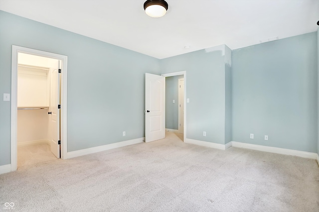 unfurnished bedroom featuring a closet, a walk in closet, and light colored carpet