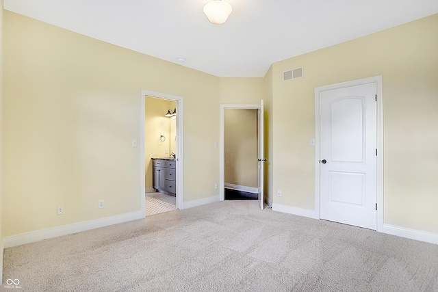 unfurnished bedroom with a closet, light carpet, and ensuite bath