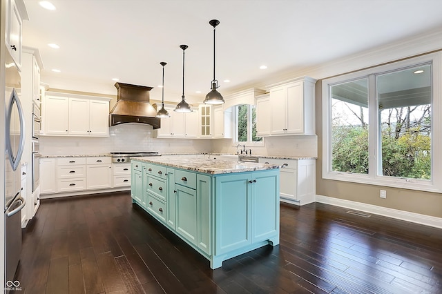 kitchen featuring a wealth of natural light, premium range hood, light stone counters, and a center island