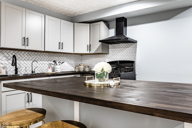 kitchen with backsplash, wall chimney range hood, black range with gas cooktop, and wooden counters