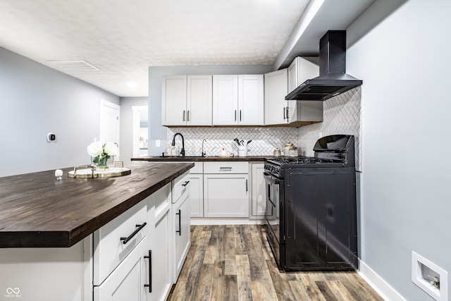 kitchen with wooden counters, wall chimney exhaust hood, wood-type flooring, black gas stove, and white cabinetry