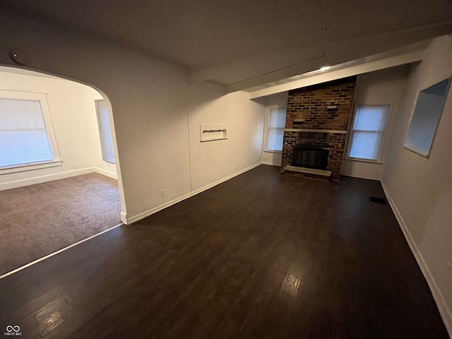 unfurnished living room featuring a brick fireplace and dark hardwood / wood-style flooring