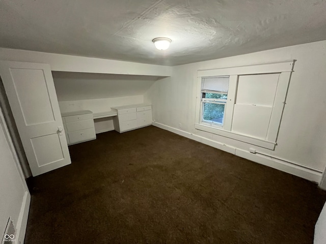 bonus room featuring built in desk and dark carpet