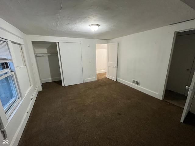 unfurnished bedroom with dark colored carpet and a closet