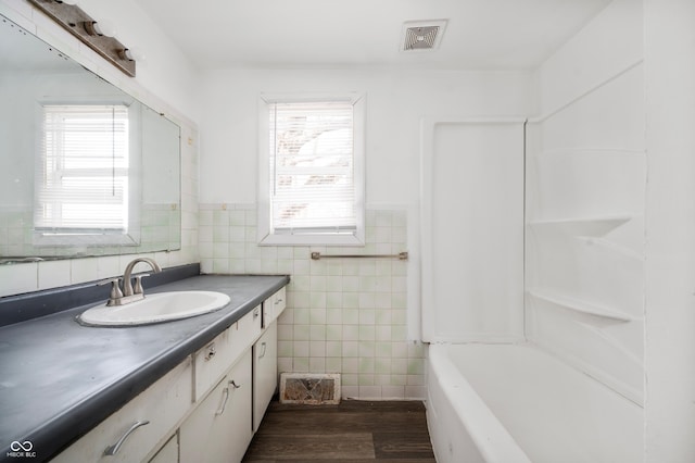 bathroom with tile walls, hardwood / wood-style floors, vanity, and shower / bathtub combination