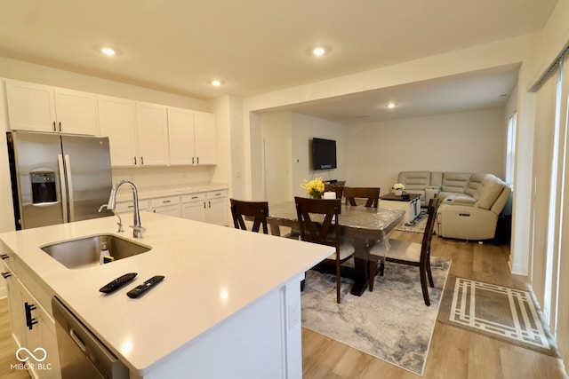 kitchen with stainless steel appliances, a center island with sink, sink, white cabinetry, and light hardwood / wood-style flooring