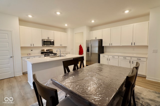 kitchen with stainless steel appliances, light hardwood / wood-style floors, and an island with sink