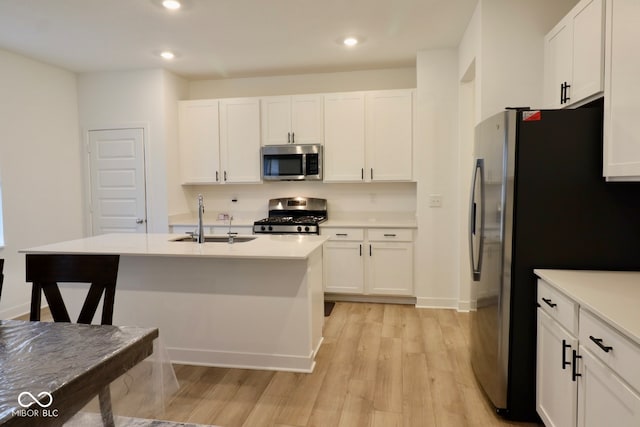 kitchen featuring a center island with sink, white cabinetry, appliances with stainless steel finishes, sink, and light hardwood / wood-style floors