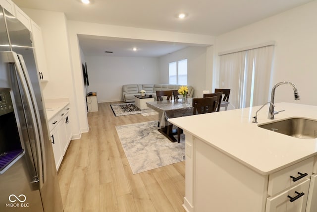 kitchen with a center island with sink, sink, white cabinets, stainless steel fridge with ice dispenser, and light wood-type flooring