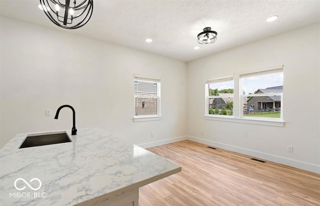 kitchen with light stone counters, a textured ceiling, sink, light hardwood / wood-style flooring, and an inviting chandelier