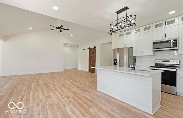 kitchen with white cabinetry, sink, stainless steel appliances, a barn door, and an island with sink