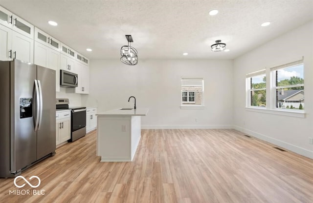 kitchen with a center island with sink, white cabinets, decorative light fixtures, and appliances with stainless steel finishes