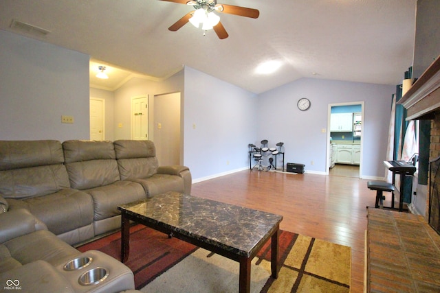 living room with wood-type flooring, crown molding, vaulted ceiling, a brick fireplace, and ceiling fan