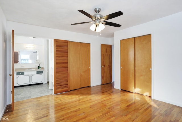 unfurnished bedroom featuring ceiling fan, light hardwood / wood-style floors, multiple closets, and sink