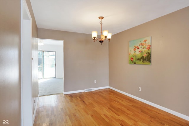 empty room with hardwood / wood-style flooring and an inviting chandelier