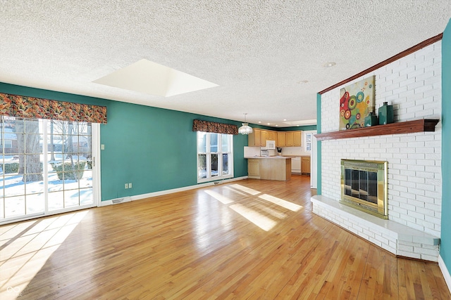 unfurnished living room featuring light wood-type flooring, a brick fireplace, a skylight, and a textured ceiling