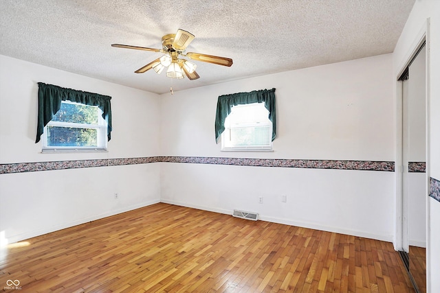 spare room with ceiling fan, plenty of natural light, wood-type flooring, and a textured ceiling