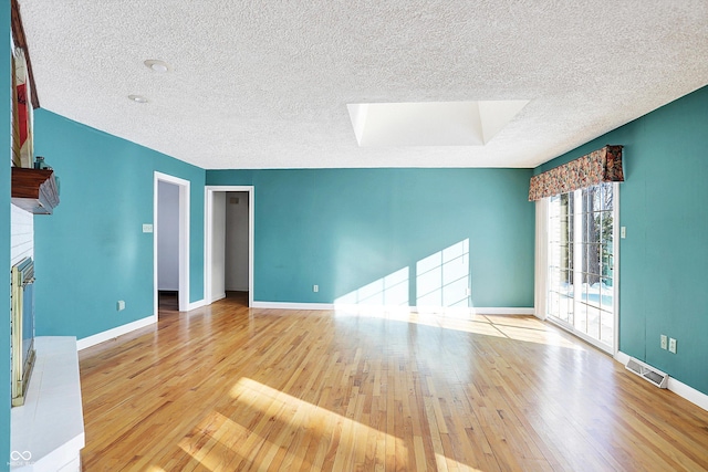 unfurnished room featuring a brick fireplace, light hardwood / wood-style floors, a textured ceiling, and a skylight