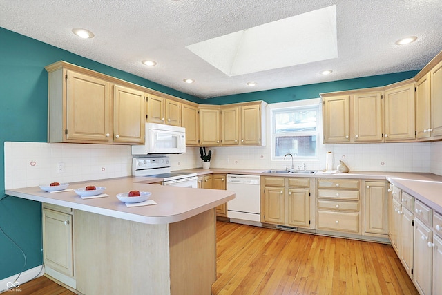 kitchen featuring white appliances, a skylight, sink, kitchen peninsula, and light wood-type flooring