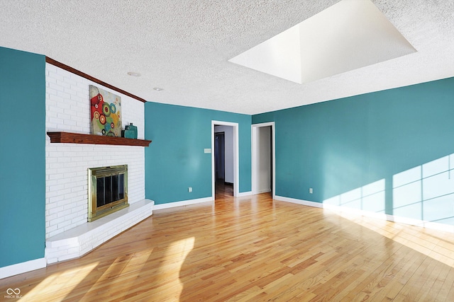 unfurnished living room featuring light wood-type flooring, a brick fireplace, and a textured ceiling